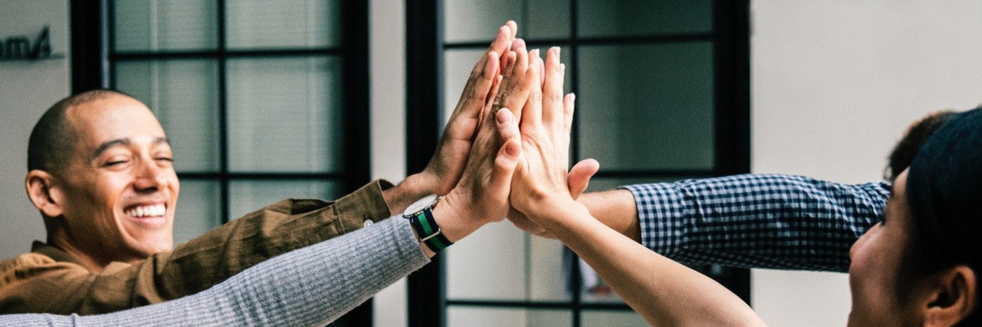 An image of a few happy people sitting around a table and high-fiving each other.